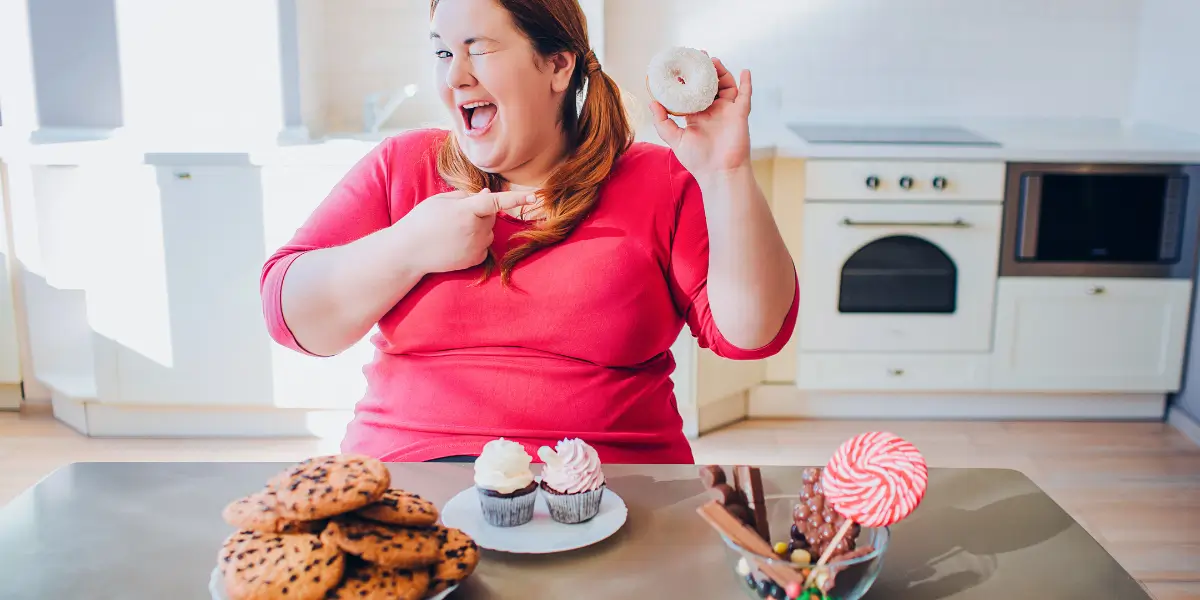 Mulher sorrindo com doces sobre a mesa, simbolizando erros no emagrecimento saudável.
